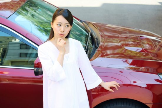 車の前に立って疑問を感じている女性